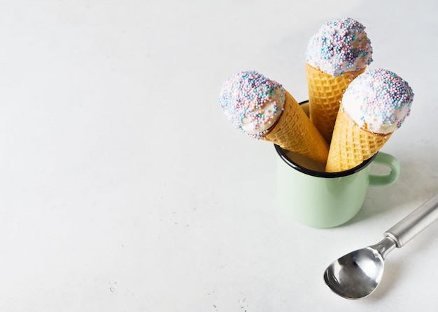 Cuillère à crème glacée à la vanille blanche dans un cône gaufré avec des pépites dans une tasse sur fond gris clair