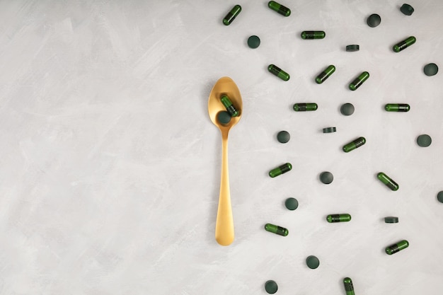 Cuillère dorée avec des capsules d'additifs alimentaires naturels avec de la poudre de moringa et des comprimés de spiruline verte