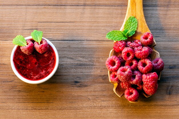 Cuillère à framboise et bol de confiture de framboises sur fond de bois,