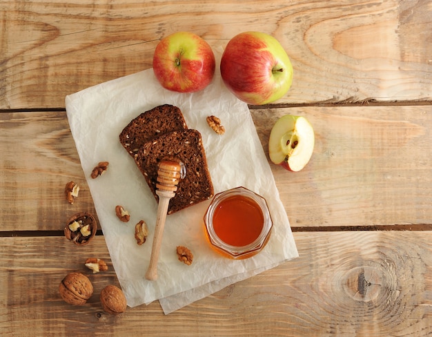 Cuillère à miel avec du pain, des pommes, des noix sur du papier kraft