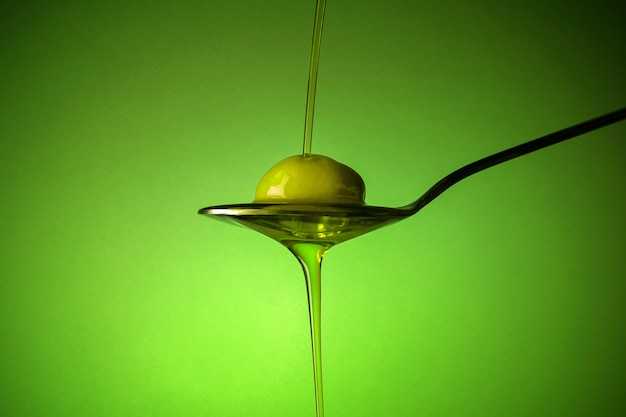 Une cuillère avec une olive sous une chute d'huile sur fond vert