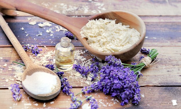 Cuillère pleine de flocons de savon avec huile essentielle et bouquet de fleurs de lavande et de bicarbonate de sodium sur une surface en bois