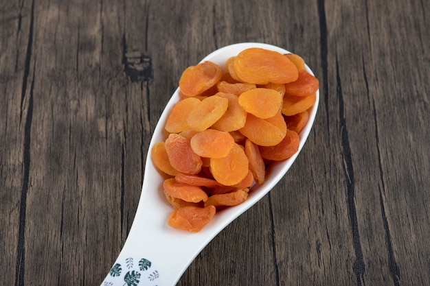 Une cuillère pleine de fruits d'abricots secs sains sur une table en bois.