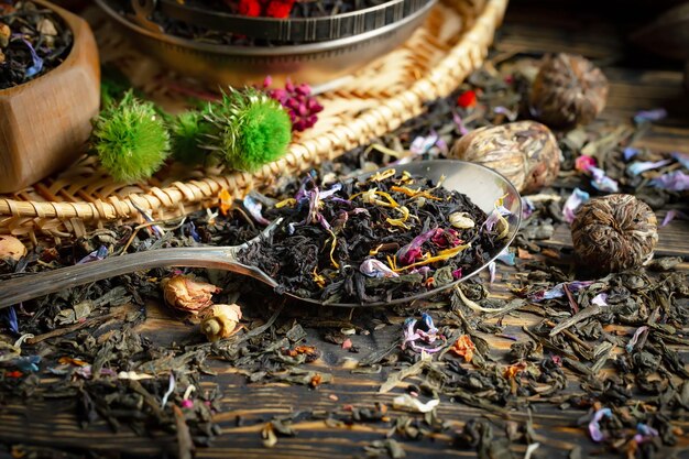 Photo une cuillère pleine de thé est posée sur une table avec d'autres feuilles de thé et fleurs.