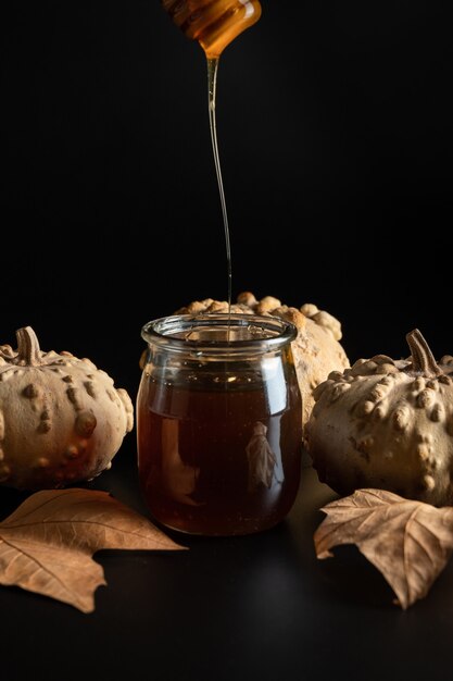 Cuillère à verser le miel dans un bocal en verre, les citrouilles et les feuilles d'automne