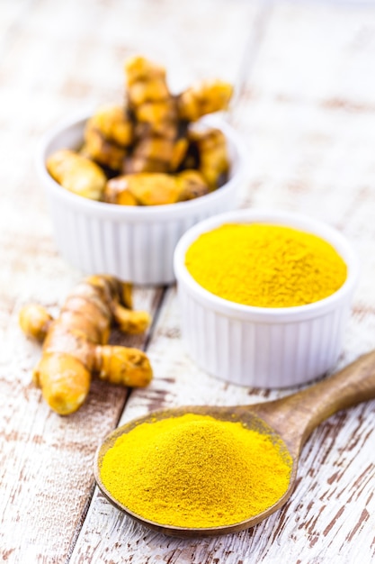 Photo cuillerée de racines de curcuma en poudre, curcuma dans un bol en bois sur table blanche