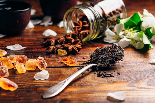 Cuillerée de thé, de fleurs de pommier, de sucre et d'étoile d'anis éparse sur une table en bois.