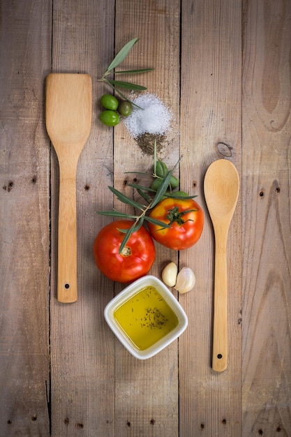 Cuillères en bois avec une cuillère en bois et une cuillère en bois avec de l'huile d'olive et une tomate dessus.