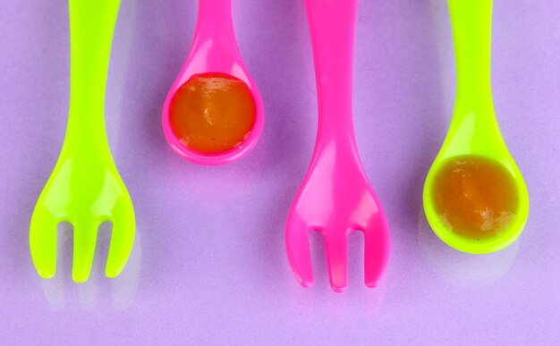 Cuillères et fourchettes de couleur pour aliments pour bébés sur table violette