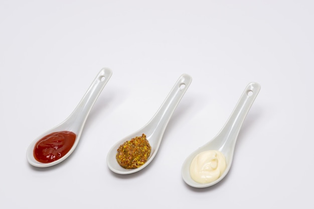 cuillères trois sauces ketchup mayonnaise moutarde fond blanc