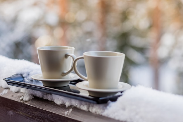 Cuire du café chaud à la vapeur dans deux tasses, enfoui dans la neige, sur un balcon, par un beau matin d'hiver. Petit déjeuner pour deux. Hiver douillet