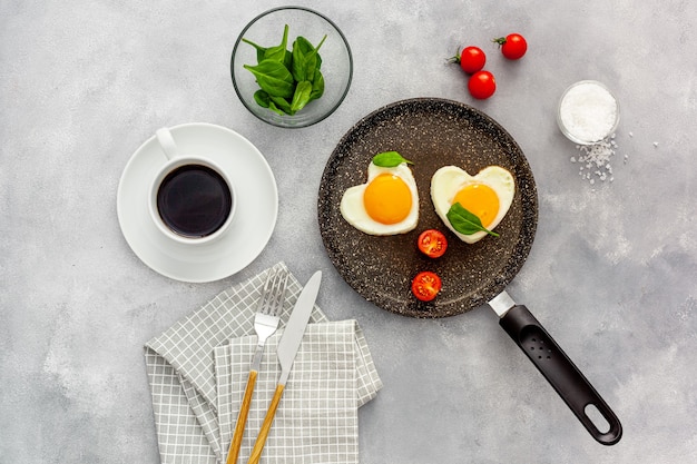 Cuire des œufs au plat en forme de cœur dans une poêle avec des tomates et des légumes verts