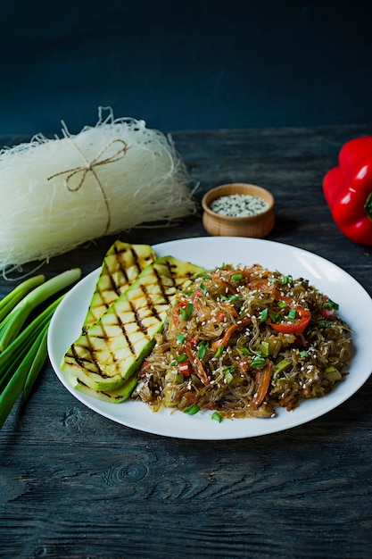 Cuisine asiatique. Nouilles de cellophane décorées de légumes, de légumes verts. Funchoza. Nutrition adéquat. Nourriture saine. Vue d'en-haut. Fond en bois foncé.