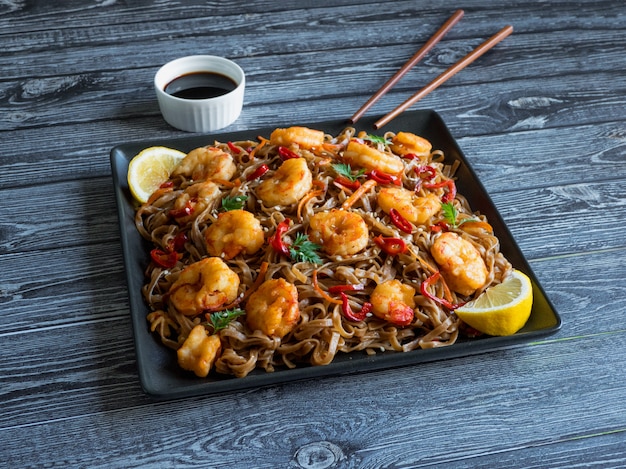 Cuisine asiatique nouilles udon aux crevettes frites, sésame et poivre gros plan sur une plaque sur la table en bois.