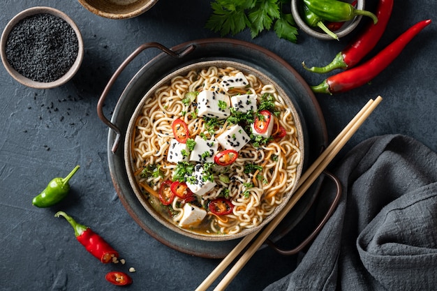 Cuisine asiatique, ramen au tofu et légumes dans un bol en céramique sur fond sombre, vue du dessus