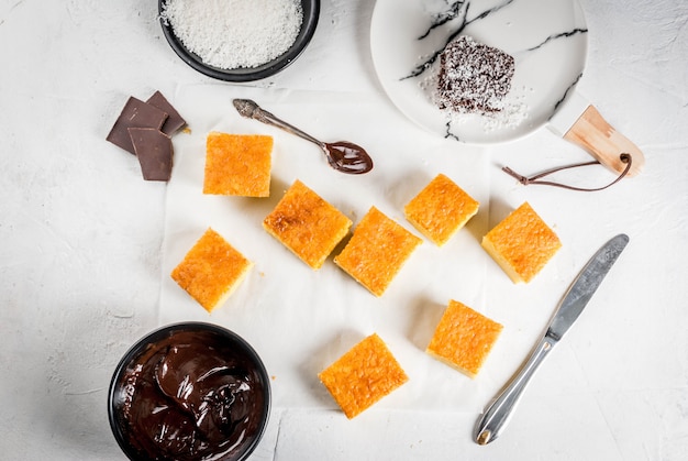 Cuisine australienne. Préparation du dessert traditionnel australien Lamington: biscuit au chocolat avec poudre de rasage à la noix de coco. Vue de dessus. Tableau blanc.