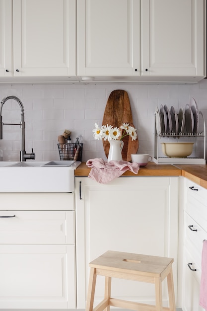 Cuisine blanche moderne avec un bouquet de fleurs de camomille dans une cruche et divers trucs de cuisine