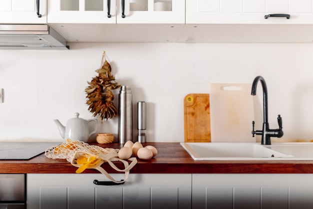 Cuisine blanche avec des oeufs et boîte-cadeau Carte de Joyeuses Pâques avec des oeufs en bois Shopper en maille avec des oeufs