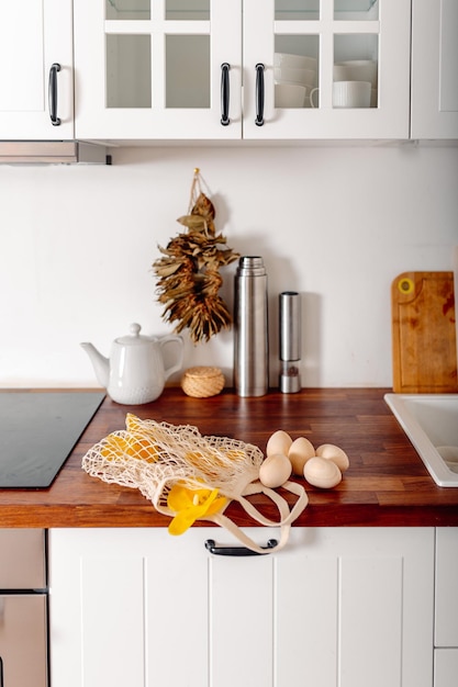 Cuisine blanche avec des oeufs et boîte-cadeau Carte de Joyeuses Pâques avec des oeufs en bois Shopper en maille avec des oeufs