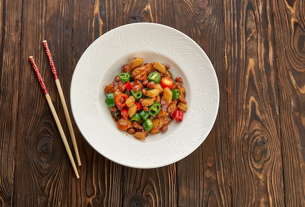 La cuisine chinoise, poulet kung pao dans une assiette blanche avec des baguettes sur une table en bois, vue de dessus et copiez l'espace