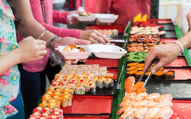 cuisine, cuisine asiatique, vente et concept alimentaire - gros plan des mains avec des pinces prenant des sushis au marché de rue