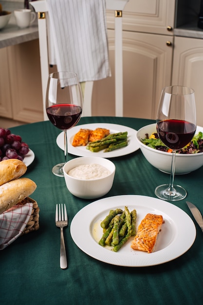 Cuisine européenne. Pavé de saumon aux asperges, salade de légumes, sauce, raisins et pain avec verres de vin rouge. Dîner pour deux dans la cuisine