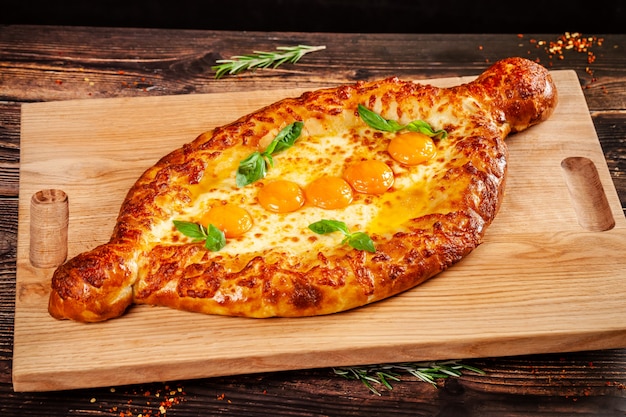 Cuisine géorgienne. Gros khachapuri avec 5 jaunes d'oeuf, sur une planche de bois. Un plat dans un restaurant pour une grande entreprise. Espace de copie de l'image de fond