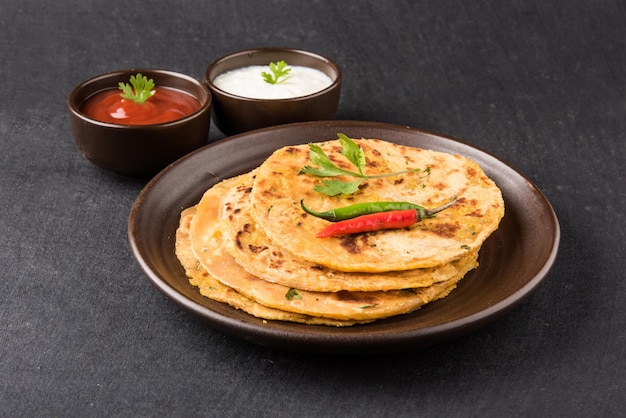 Cuisine indienne traditionnelle Aloo paratha ou pain plat farci de pommes de terre. servi avec du ketchup et du lait caillé sur fond coloré ou en bois. Mise au point sélective