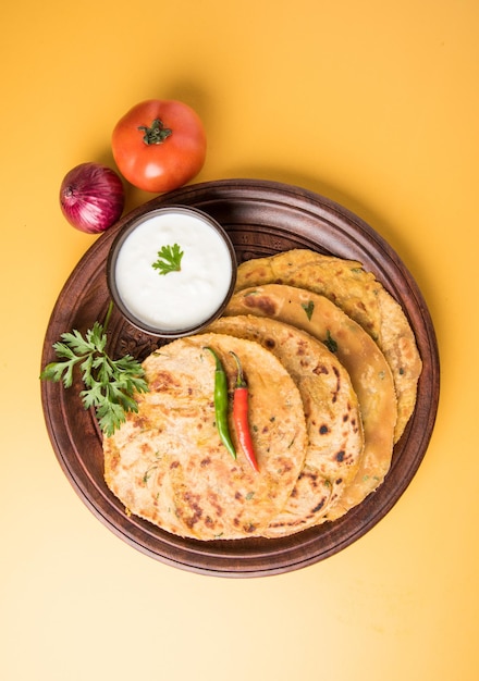 Cuisine indienne traditionnelle Aloo paratha ou pain plat farci de pommes de terre. servi avec du ketchup et du lait caillé sur fond coloré ou en bois. Mise au point sélective