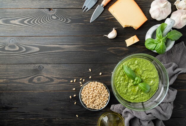 Cuisine italienne. Préparation d'une sauce pesto italienne maison. Pesto frais dans un bol avec des ingrédients, vue de dessus à plat sur une table en bois noir, espace pour copie