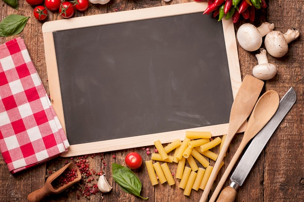 Cuisine italienne. Tomates, basilic, pâtes et tableau noir pour votre recette sur table de cuisine en pierre. Vue de dessus avec espace de copie