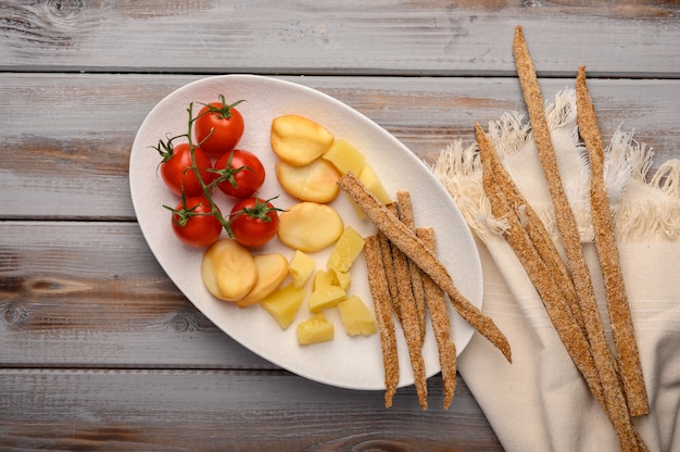 La cuisine italienne traditionnelle est le pain grissini avec du prosciutto, du fromage et des tomates aux herbes sur une assiette sur un fond en bois.