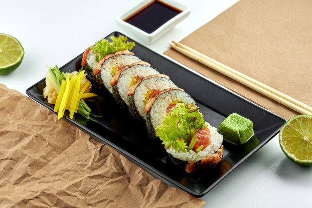 Cuisine japonaise classique - rouleau de sushi futomaki avec saumon cuit et légèrement salé, concombre, servi dans une assiette noire sur une assiette blanche. Gros plan, mise au point sélective