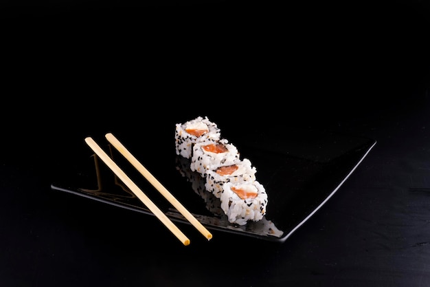 Cuisine japonaise sur plaque noire avec quatre sushis au saumon et fromage à la crème et baguettes en vue d'angle