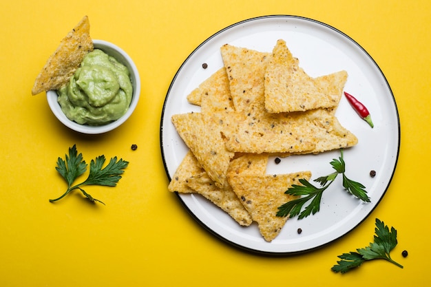 Cuisine mexicaine traditionnelle Guacamole avec chips de maïs sur fond jaune.