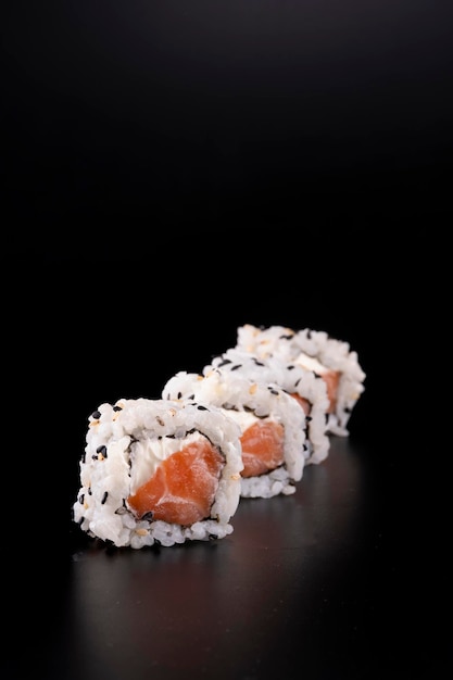 Cuisine orientale japonaise avec quatre rouleaux de sushi au saumon côte à côte et fromage à la crème vus au premier rang sur fond noir en gros plan arrière-plan flou