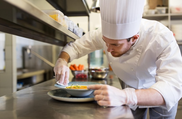 cuisine, profession et concept de personnes - chef cuisinier heureux servant une assiette de soupe dans la cuisine d'un restaurant