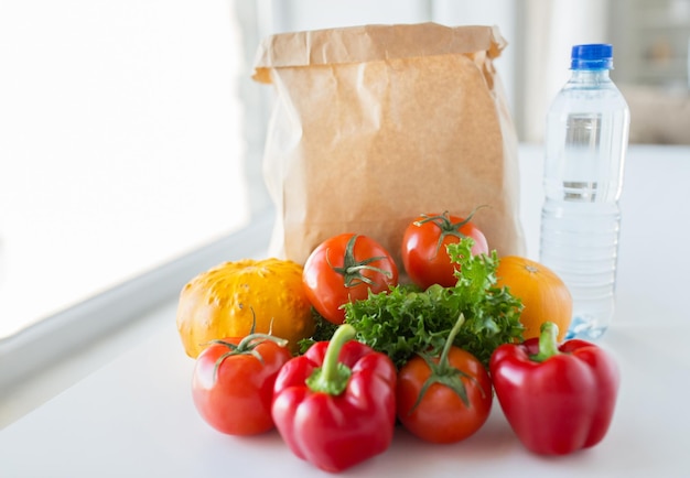 cuisine, régime alimentaire, nourriture végétarienne et concept d'alimentation saine - gros plan d'un sac en papier avec des légumes juteux mûrs frais et une bouteille d'eau sur la table de la cuisine à la maison