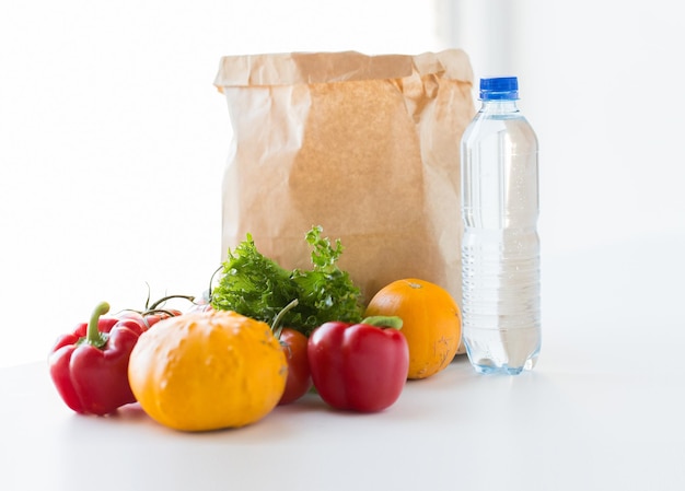 cuisine, régime alimentaire, nourriture végétarienne et concept d'alimentation saine - gros plan d'un sac en papier avec des légumes juteux mûrs frais et une bouteille d'eau sur la table de la cuisine à la maison