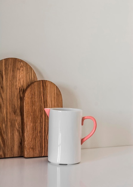 Une cuisine simple, des planches à couper en bois et un pot en céramique sur une table blanche.