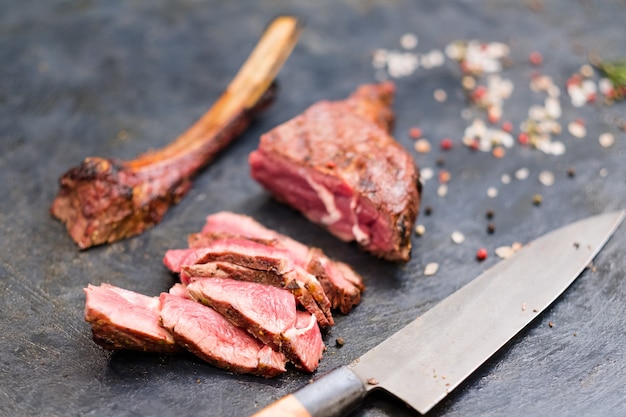 Cuisine de steakhouse. Steak de cow-boy. Gros plan de viande de boeuf grillée en tranches, d'os et de couteau.