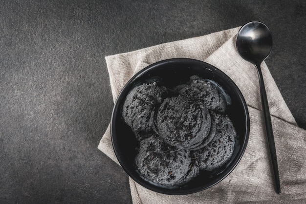 Cuisine tendance. Glace noire au sésame noir, dans un bol noir sur une table en pierre noire, avec une cuillère.