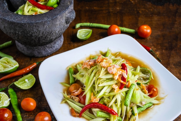 Cuisine thaïlandaise, salade de papaye et salade de papaye dans un plat avec une portion sur une table en bois.