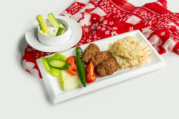 Cuisine turque traditionnelle Izgara Kofte avec raïta de riz et salade dans un plat isolé sur une nappe colorée vue de dessus sur fond gris