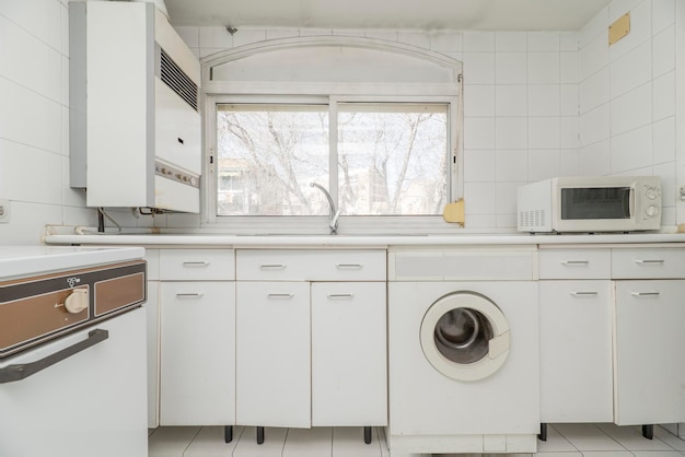 Cuisine vintage blanche avec fenêtre avec vue électroménagers blancs et sols en grès de la même couleur