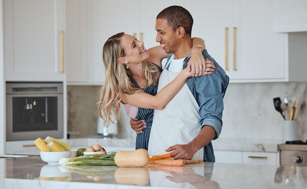 Cuisiner l'amour ou un couple câlin dans une cuisine avec une alimentation saine dans une relation interraciale ou un mariage à la maison Légumes carottes ou femme heureuse étreignant un partenaire romantique préparant un dîner