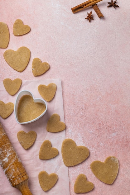 Cuisiner des biscuits pour la saint-valentin avec des ingrédients sur fond rose