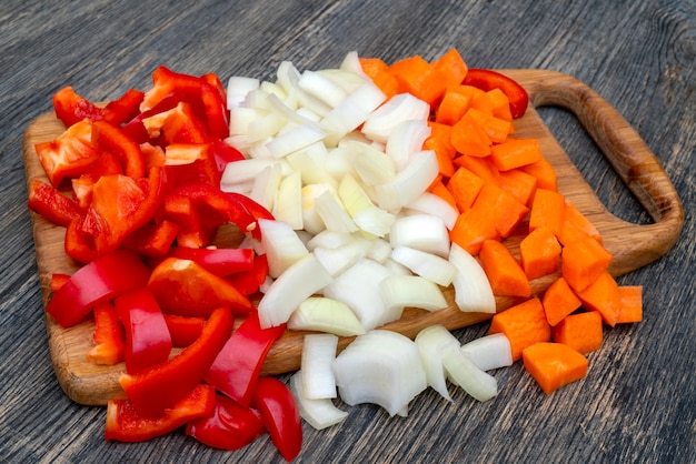 Cuisiner dans la cuisine. Couper les oignons, les carottes, le poivron bulgare.