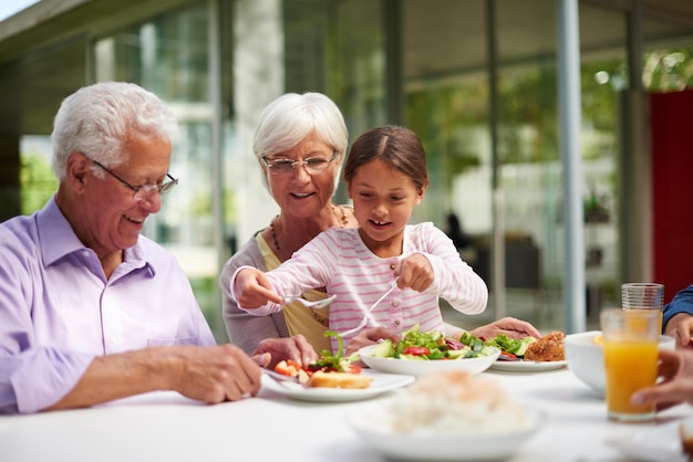 Cuisiner pour grand-mère et grand-père Photo d'une petite-fille assise avec ses grands-parents tout en savourant un repas à l'extérieur