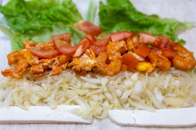 Cuisiner un rouleau de restauration rapide fait maison en gros plan. chou, crevettes frites et tomates avec du fromage sur du pain pita. une collation copieuse rapide et délicieuse pour l'école ou le travail